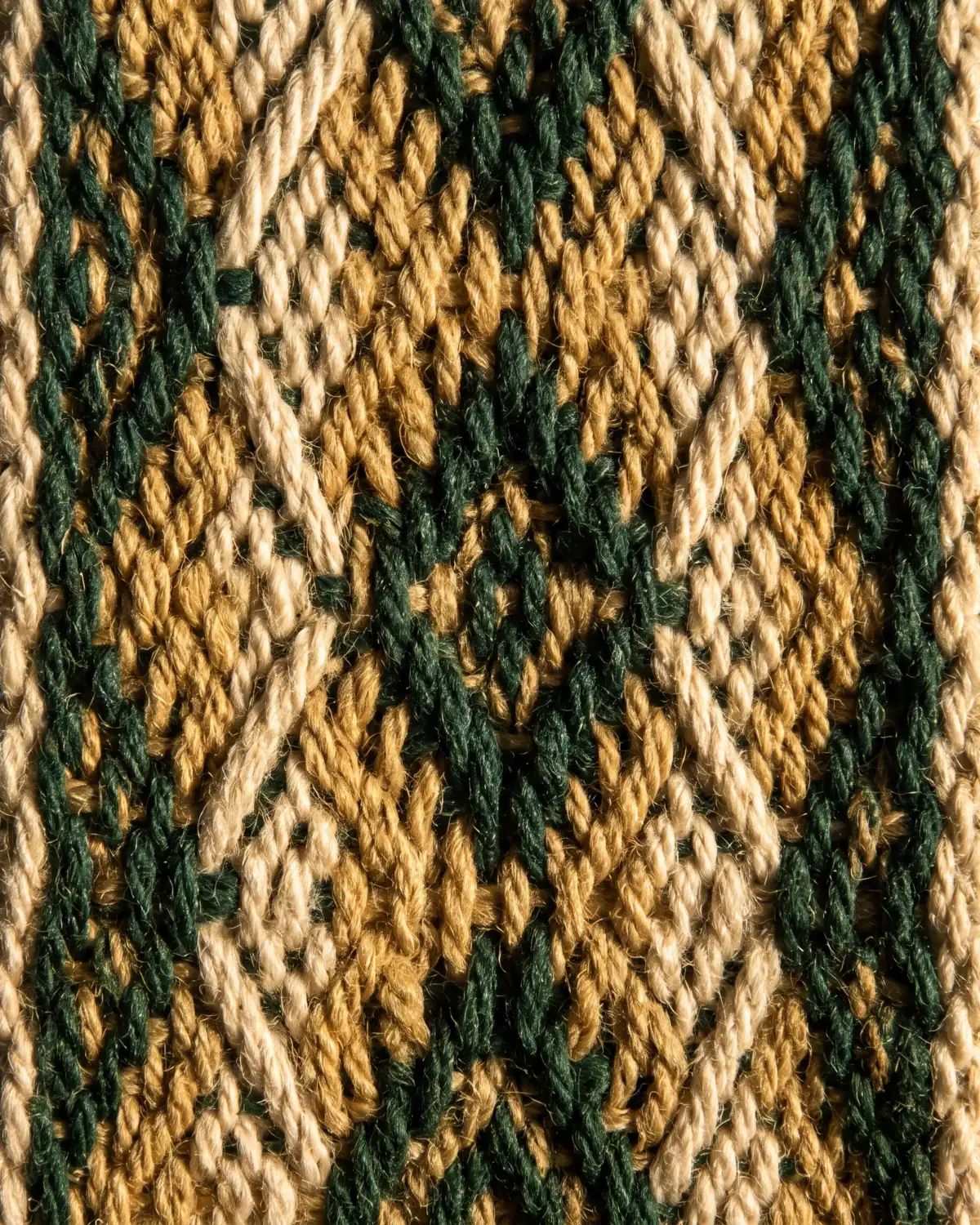 A handwoven textile in gold, cream and deep green thread, its repeating diamond motif raised by low side light.